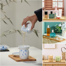 تحميل الصورة في عارض المعرض، Tea being poured from a white teapot with blue patterns into a white cup on a wooden coaster.