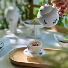 Load image into Gallery viewer, Tea being poured from a white teapot with blue butterfly designs into a matching cup on a wooden tray.