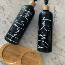 تحميل الصورة في عارض المعرض، Two black bottles labeled 'Hand Wash' and 'Dish Soap' on a marble surface with wooden lids.