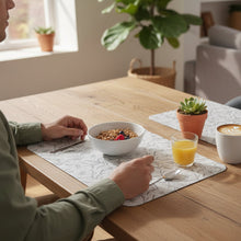 Load image into Gallery viewer, A rectangular mouse pad with rounded corners, featuring a light beige background with a dark gray floral and leaf pattern, resting on a wooden desk.