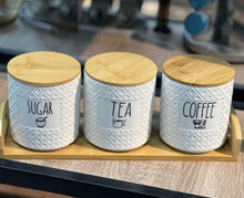 Load image into Gallery viewer, Three white canisters with wooden lids labeled 'Sugar', 'Tea', and 'Coffee' on a wooden tray.
