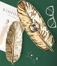 تحميل الصورة في عارض المعرض، Gold feather-shaped bookends on a green background with a magazine and glasses.