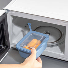 Load image into Gallery viewer, Person holding a blue silicone food container with food inside an open microwave.