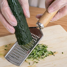 Load image into Gallery viewer, Person grating a cucumber using a stainless steel cheese grater with a wooden handle on a cutting board.