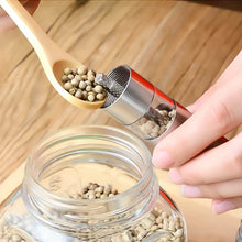 Load image into Gallery viewer, Person using a spoon to add peppercorns to a stainless steel pepper grinder, showcasing adjustable coarseness.