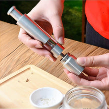 Load image into Gallery viewer, Person assembling a stainless steel pepper and spice grinder on a wooden table, showcasing its adjustable coarseness feature.