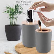 تحميل الصورة في عارض المعرض، Gray bathroom set with soap dispenser, toothbrush holder, and bamboo toothbrush on a wooden tray.