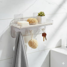 تحميل الصورة في عارض المعرض، Clear acrylic wall-mounted bathroom shelf with suction cups, shown holding a small potted succulent, sponge, bar of soap, hanging sponge, keys, and a gray towel against a white marble wall.