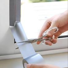 Load image into Gallery viewer, Person using scissors to cut a roll of tape on a window