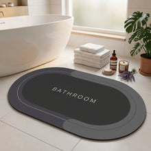 Load image into Gallery viewer, Dark grey oval bath mat printed BATHROOM, with a foot stepping on it