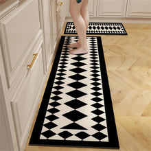 تحميل الصورة في عارض المعرض، A set of black and white geometric-patterned anti-slip mats placed on a kitchen floor, with a person's feet visible, indicating the use of the mat for safety and stability.