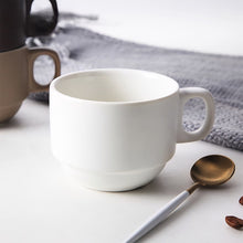 Load image into Gallery viewer, White mug on a white surface with a gold spoon and gray towel in the background
