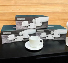 Load image into Gallery viewer, Set of white coffee cups and saucers with packaging on a black surface and wooden background