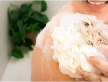 Load image into Gallery viewer, Person using an exfoliating bath sponge in the shower, surrounded by bubbles and greenery.