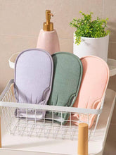 Load image into Gallery viewer, Set of three exfoliating loofah gloves in pastel colors displayed in a basket with a soap dispenser and plant.