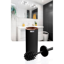 Load image into Gallery viewer, A black cylindrical toilet brush with a metallic copper-toned top and a black brush head, shown in front of a blurred bathroom background featuring a sink, mirror, and toilet.