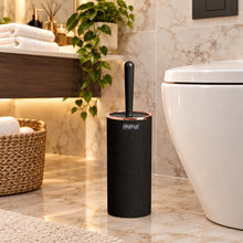 Load image into Gallery viewer, A black cylindrical toilet brush holder with a matching brush standing upright, shown in front of a bathroom scene with a sink, mirror, and toilet.