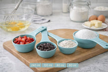 تحميل الصورة في عارض المعرض، Four light blue measuring cups filled with ingredients (strawberries, chocolate chips, flour, sugar) arranged on a wooden cutting board in a kitchen setting, with volume labels 240 ml, 120 ml, 80 ml, and 60 ml shown at the bottom.