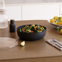 تحميل الصورة في عارض المعرض، Black bowl with salad on a wooden table with lemon slices and cutlery.