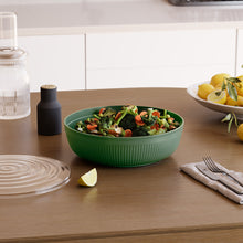 تحميل الصورة في عارض المعرض، Green salad bowl with a salad on a wooden table with lemons and a glass bottle in the background.