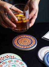 Load image into Gallery viewer, Person holding a glass of iced drink with decorative coasters on a dark surface