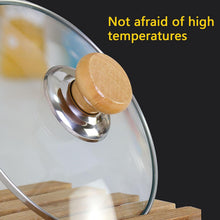 تحميل الصورة في عارض المعرض، A close-up of a clear glass pot lid with a round light wood knob and shiny silver metal rim, resting on a wooden surface against a dark background. Yellow text in the upper right reads 'Not afraid of high temperatures'.