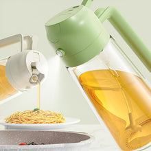 تحميل الصورة في عارض المعرض، A close-up of a light green and clear oil dispenser bottle pouring oil onto spaghetti on a plate, with another bottle in the foreground and a pan at the bottom on a clean, light background.