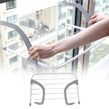 تحميل الصورة في عارض المعرض، Person using a gray clothes drying rack against a window with a cityscape view.