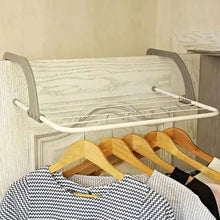 Load image into Gallery viewer, Clothing rack with clothes on hangers against a neutral wall.