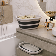 Load image into Gallery viewer, Collapsible black and white striped bathtub on a bathroom counter with toiletries.