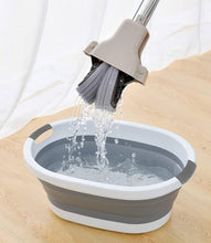 Load image into Gallery viewer, Collapsible bucket with a brush being rinsed under water on a wooden surface.