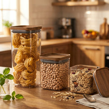 Load image into Gallery viewer, Set of glass storage jars with wooden lids containing pasta, beans, and grains on a wooden surface.