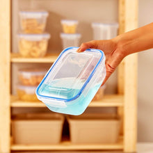 Load image into Gallery viewer, Hand holding a clear plastic container with blue lid in front of a wooden shelf with storage bins.