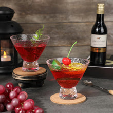 Load image into Gallery viewer, Two red cocktails in martini glasses with garnishes on a dark surface, accompanied by grapes and a bottle of wine.