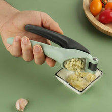 Load image into Gallery viewer, A person holding a green and black heavy-duty stainless steel garlic press with crushed garlic visible in the press.