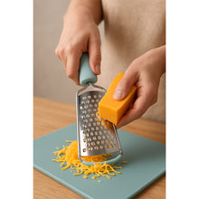 Load image into Gallery viewer, Person using a cheese grater to shred cheese on a cutting board.