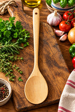 Load image into Gallery viewer, A light natural wood kitchen spoon with a hanging retail card, placed on a dark brown wooden table.