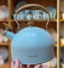 Load image into Gallery viewer, Light blue kettle with wooden handle held in front of a blurred background with 'Hekal Gallery' branding.