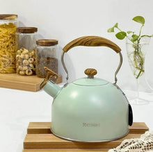 Load image into Gallery viewer, Mint green kettle with wooden handle on a wooden stand, with jars and a plant in the background.