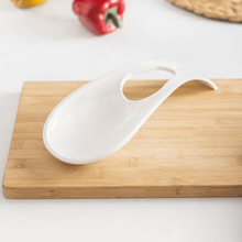 تحميل الصورة في عارض المعرض، White ladle on a wooden cutting board with peppers and a woven mat in the background.