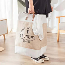 Load image into Gallery viewer, A laundry bag with beige and brown colors, featuring leather handles and the text 'WASH • DRY • IRON • LAUNDRY • DELUXE' printed on the front.