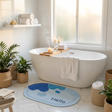 Load image into Gallery viewer, Light blue oval bath mat with a blue wave design and Hello print