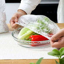 Load image into Gallery viewer, Person using plastic food storage cover over salad bowl with fresh vegetables, demonstrating easy food preservation.