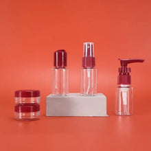 Load image into Gallery viewer, Set of clear cosmetic bottles with red caps on an orange background