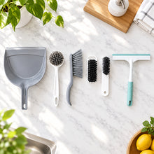 تحميل الصورة في عارض المعرض، A set of household cleaning tools arranged on a light gray wood-grain surface, including a gray dustpan, a white-handled brush, a gray scrubber, two small black-bristled brush heads, and a squeegee with a white and mint green handle.
