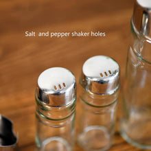 تحميل الصورة في عارض المعرض، Two glass salt and pepper shakers with metal tops on a wooden surface.