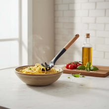 Load image into Gallery viewer, Bowl of pasta with a wooden fork, tomatoes, and basil on a kitchen counter.