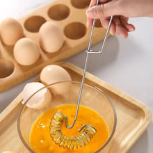 Load image into Gallery viewer, Person using a metal egg separator to separate yolks from whites in a glass bowl, with eggs and a wooden tray in the background.