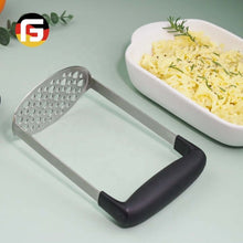 تحميل الصورة في عارض المعرض، Metal potato masher with black handle on a light green background, next to a dish of mashed potatoes.