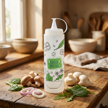 تحميل الصورة في عارض المعرض، A clear plastic squeeze sauce bottle with a white cap and handle, decorated with green and black food illustrations and a green label that reads 'SAUCE BOTTLE'.